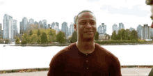 a man in a maroon shirt is standing in front of a city skyline .