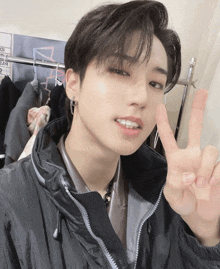 a young man giving a peace sign in front of a clothes rack