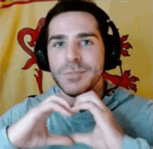 the man is wearing headphones and making a heart shape with his hands .