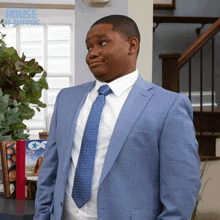 a man in a blue suit and tie is standing in front of a staircase with the words house approved on the bottom