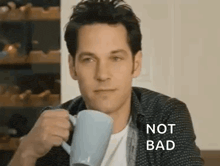 a man is sitting at a table drinking a cup of coffee and making a funny face .