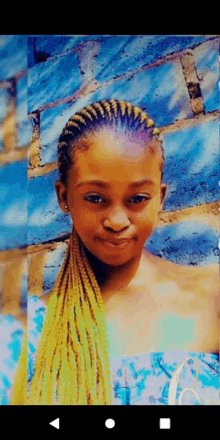 a young girl with braids in her hair is smiling in front of a blue brick wall .