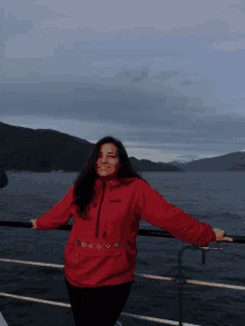 a woman wearing a red columbia sweatshirt stands on a boat with her arms outstretched