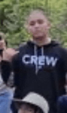 a man in a crew hoodie is standing in a crowd of people .