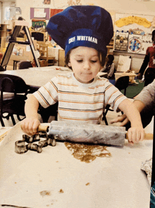 a little boy wearing a chef whitman hat is rolling out dough