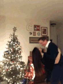 a man and woman are dancing in front of a christmas tree with the letter c on the wall behind them