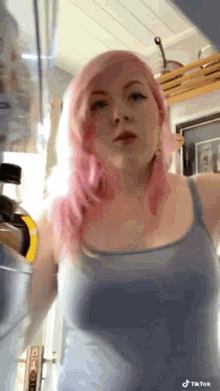 a woman with pink hair is standing in a kitchen with a bottle of alcohol in her hand .