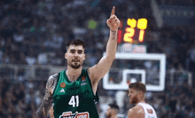 a basketball player wearing a green jersey with the number 41 on it is pointing up