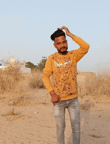 a man wearing a yellow pepe jeans sweatshirt is standing in the desert