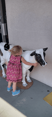 a little girl in a pink dress petting a black and white cow statue