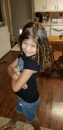 a little girl with curly hair is standing with her arms crossed in a kitchen
