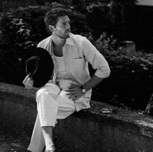 a man sitting on a wall holding a hat