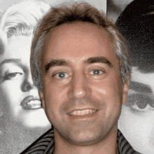 a man smiles in front of a marilyn monroe portrait