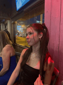 a woman in a black top sits in front of a window with a sign that says ' a ' on it