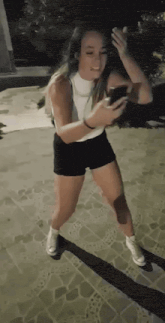 a woman in shorts and converse shoes is dancing while looking at her phone