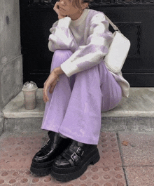 a woman wearing purple pants and a sweater is sitting on steps with a cup of coffee in her hand