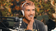 a man with pink hair is wearing headphones and smiling in front of a microphone .