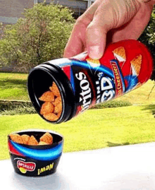 a person is pouring doritos into a cup .