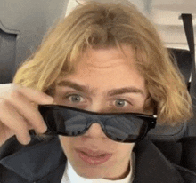 a young man with blonde hair is wearing sunglasses on a plane .