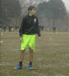 a man wearing a black jacket and neon yellow shorts stands in a field