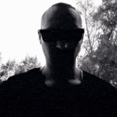 a man wearing sunglasses and a black shirt stands in front of trees
