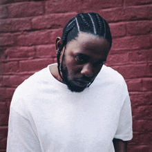 a man with braids in his hair is wearing a white shirt against a red brick wall