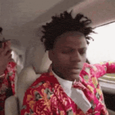 a man with dreadlocks is sitting in the back seat of a car wearing a red jacket and tie .