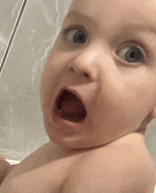 a baby with a surprised look on his face is taking a bath .