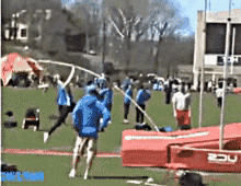 a group of people are jumping a pole in a field and one of them is wearing a blue shirt