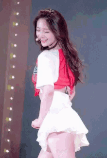 a woman in a red and white top and a white skirt is dancing on a stage .