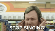 a man covering his ears in a store with the words stop singing written below him