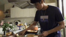 a man is cooking in a kitchen wearing a blue shirt with a picture of the ocean on it .