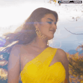 a woman in a yellow one shoulder dress is standing in front of some trees