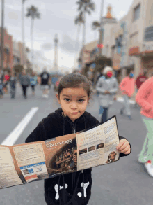 a little girl is holding a pamphlet about disney hollywood