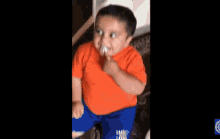 a young boy in an orange shirt and blue shorts is sitting on a tiled floor next to a chair .