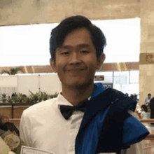 a man in a white shirt and bow tie is holding a bouquet of flowers and a diploma .