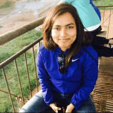 a woman wearing a blue nike jacket is sitting on a railing