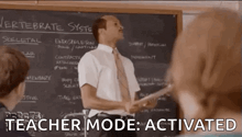 a man is standing in front of a blackboard in a classroom giving a lesson on the vertebrate system .
