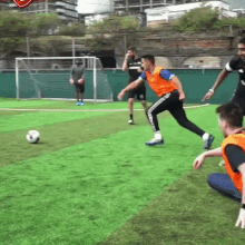 a group of men are playing soccer on a field and one of them is wearing an orange vest with the word adidas on it