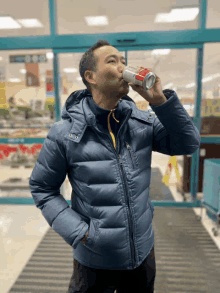 a man in a blue jacket drinks from a red can