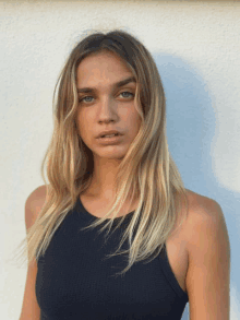 a blonde woman wearing a black tank top is standing in front of a white wall