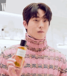 a man in a pink sweater is holding a bottle of perfume called ambre sauvage