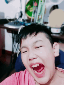 a young boy in a pink shirt is making a funny face with his mouth open