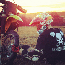 a person wearing a black shirt that says grenzoen sits next to a dirt bike