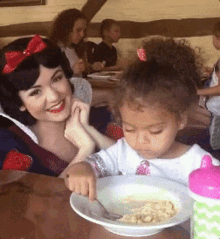 a woman and a little girl are sitting at a table with a bowl of food in front of them