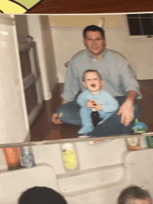 a man sits on the floor holding a baby in a blue shirt