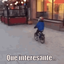 a young boy is riding a bike down a street with the words que interesante written on the sidewalk .