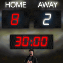 a man stands in front of a scoreboard that shows home and away