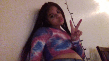 a girl with braids is giving a peace sign while wearing a tie dye shirt