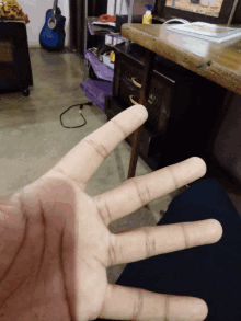 a person 's hand is shown in front of a desk and a guitar